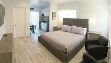 A bedroom with a bed, bedside tables, a chair, a desk, and a kitchenette.