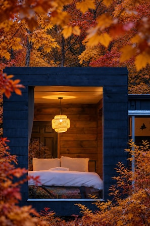 A cozy cabin with a bed and a hanging light fixture, surrounded by autumn foliage. - Field Cabin + Mountain Views + Hot Tub + Sauna (Saugerties)