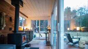 A cozy cabin interior with a wood-burning stove, a dining area, and a deck with outdoor seating. - Container Cabin in the Catskills [Field] (Saugerties)