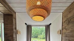 A modern room with a glass table, wooden chairs, a large window with curtains, and a unique woven light fixture. - Container Cabin in the Catskills [Field] (Saugerties)