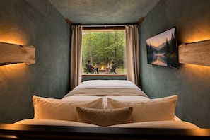 Ein Schlafzimmer mit einem großen Bett, einem Fenster mit Blick auf einen Wald und einem Gemälde an der Wand.