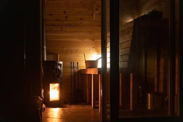 Ein Holzinnenraum mit einer zentralen Lichtquelle, Holzbalken an der Decke und einem sichtbaren Türrahmen.