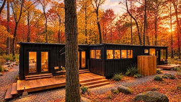 En stuga med en träveranda, en liten sittplats utomhus och utsikt över den omgivande skogen.