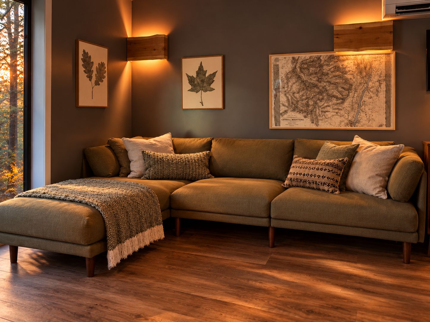 A sectional sofa with a throw blanket, framed botanical prints, and a map on the wall.