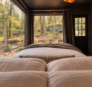 A bedroom with a large bed, a window with curtains, and a view of a forest with a deer.