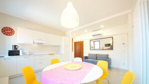 A modern kitchen with white cabinets, a dining table with a pink tablecloth, and yellow chairs. - DolceVita Apartments N. 491 (Venice)