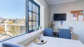 A hotel room with a large window offering a city view, a flat-screen TV mounted on the wall, and a bulletin board with notices. - Myriverplace N.6 - PORTO Riverfront Apartment With Breathtaking Views (Vila Nova de Gaia)