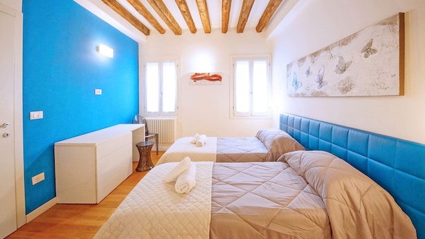 Een kamer met twee bedden, een witte ladenkast, een blauwe accentmuur, houten plafondbalken en een aan de muur hangend kunstwerk.