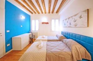 A room with two beds, a white dresser, a blue accent wall, wooden ceiling beams, and a wall-mounted artwork. - Dolcevita Apartments N. 502 (Venice)