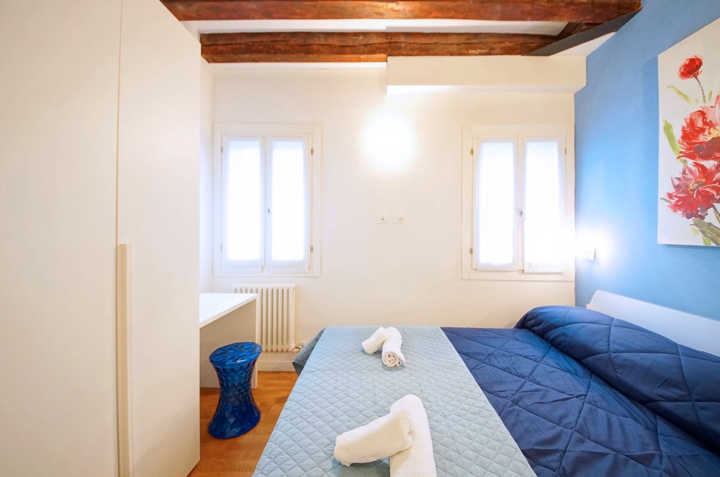 Une chambre à coucher avec un lit, un radiateur, un vase bleu et un tableau accroché au mur.