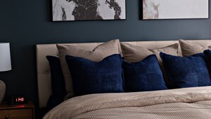 Een slaapkamer met een bed, kussens, een nachtkastje, een lamp en twee abstracte schilderijen aan de muur.