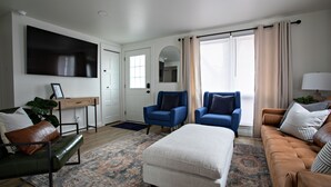 Een moderne woonkamer met een bank, twee fauteuils, een salontafel, een televisie en een bureau.
