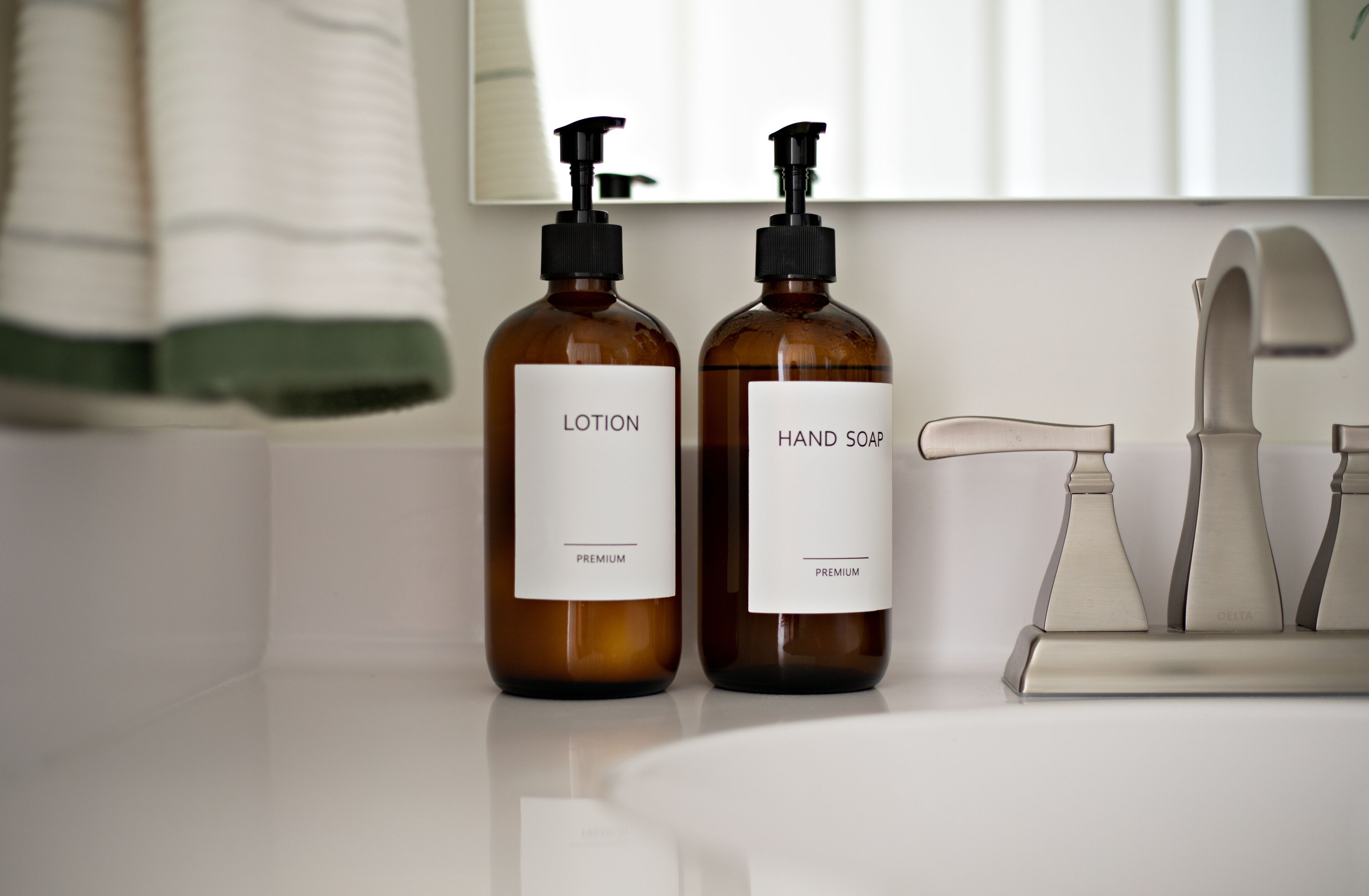 Dos botellas marrones con etiquetas que dicen 'Loción' y 'Jabón de manos' sobre un lavamanos blanco con un grifo moderno.