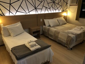 Una habitación de hotel con dos camas individuales, una mesita de noche y un televisor montado en la pared.