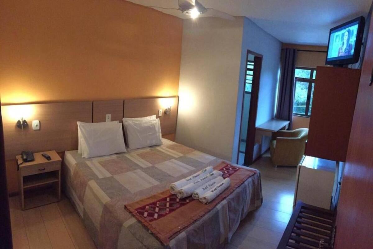 Une chambre d’hôtel comprenant un lit, une table de chevet, une télévision et un petit bureau avec une chaise.