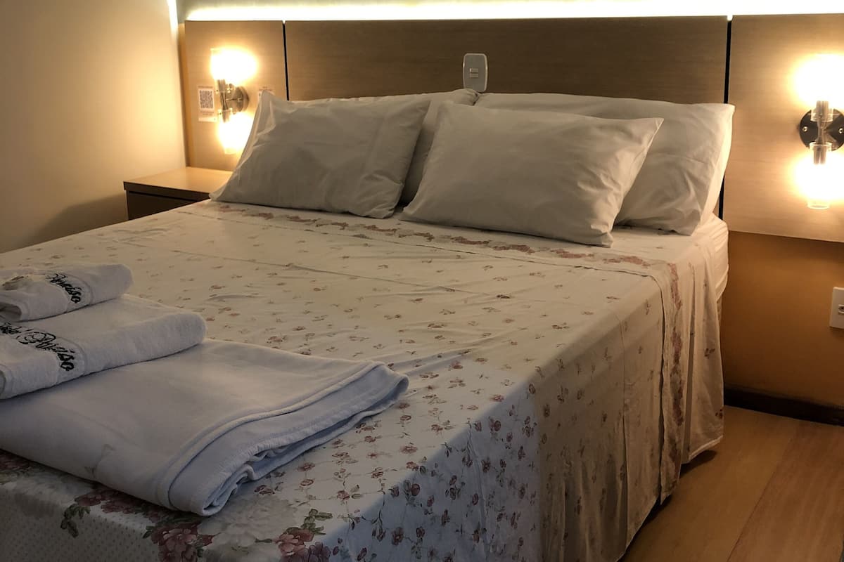 Un lit bien fait, avec une couvre-lit à motifs floraux, deux oreillers et des serviettes pliées posées sur le côté.