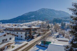 A snow-covered residential area with modern buildings, a clear road, and a mountain in the background.