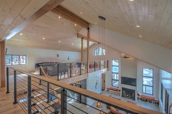 A spacious interior with a high ceiling, wooden beams, a staircase, and large windows.