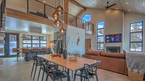 A spacious living area with a high ceiling, a dining table with chairs, a sofa, and a fireplace. - Hot Tub Haven with Panoramic View | Blue River (Breckenridge)