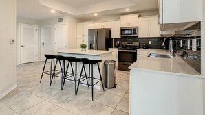 A modern kitchen with a central island, bar stools, stainless steel appliances, and white cabinetry.