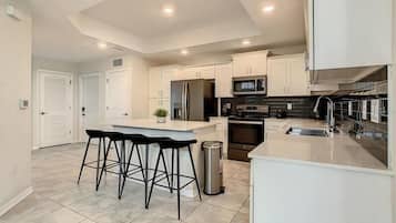 A modern kitchen with a central island, bar stools, stainless steel appliances, and white cabinetry.