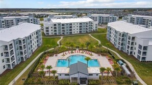 A modern apartment complex with a central courtyard featuring a swimming pool, surrounded by lush greenery and palm trees.