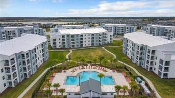 A modern apartment complex with a central courtyard featuring a swimming pool, surrounded by lush greenery and palm trees.
