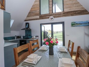 A dining room with a table set for six, wooden chairs, a vase with flowers, and a view of the outdoors through a door. - Valley View Hideaway (Llandysul)