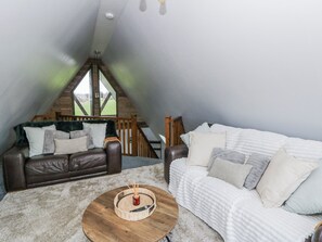A loft bedroom with a brown leather sofa, a white sofa, and a round wooden coffee table. - Valley View Hideaway (Llandysul)