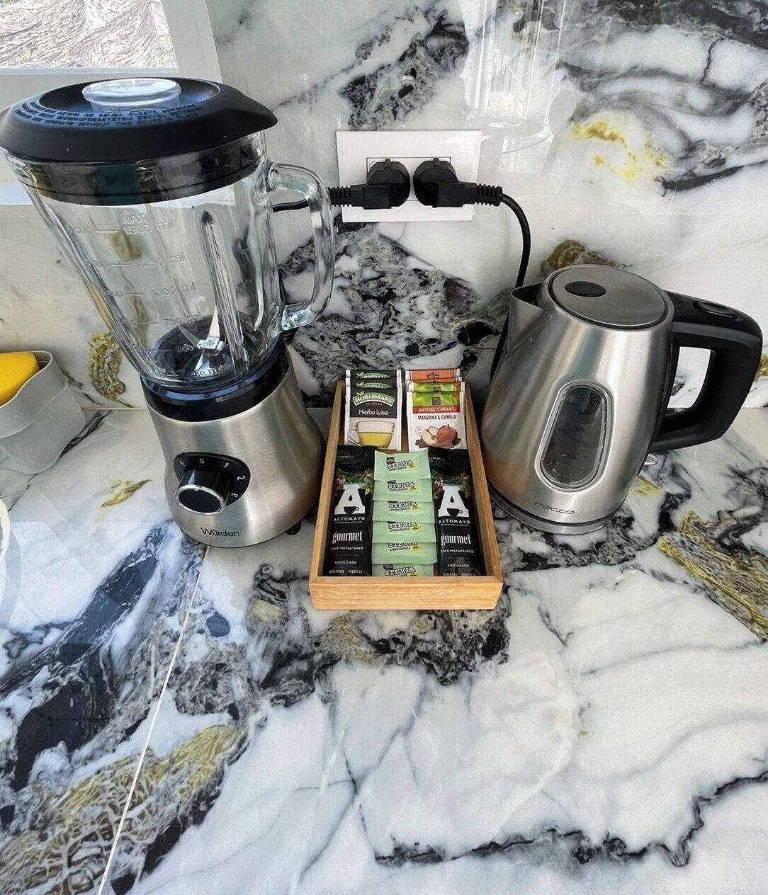 A kitchen counter with a blender, a coffee maker, and a box of gourmet tea.