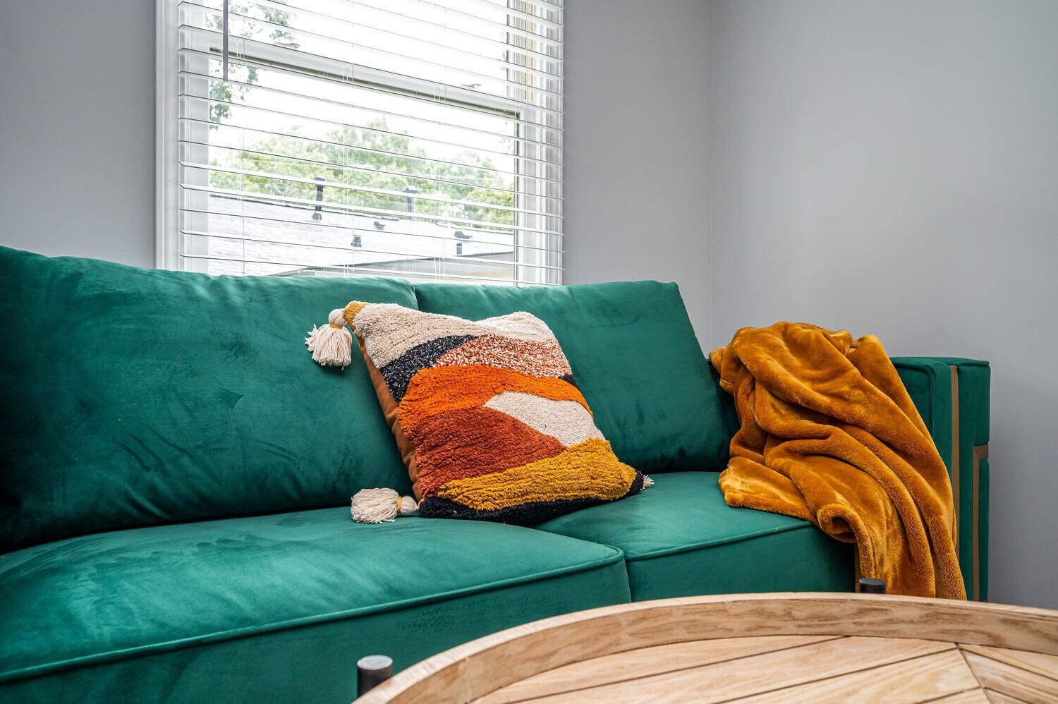 A green sofa with a colorful throw pillow and a mustard-colored blanket.