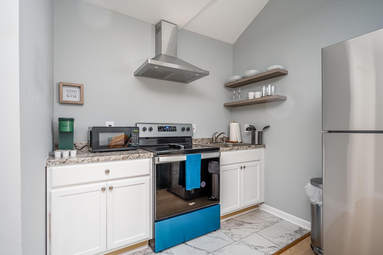 A modern kitchen with white cabinets, a stainless steel range hood, a built-in oven, a microwave, and a refrigerator.