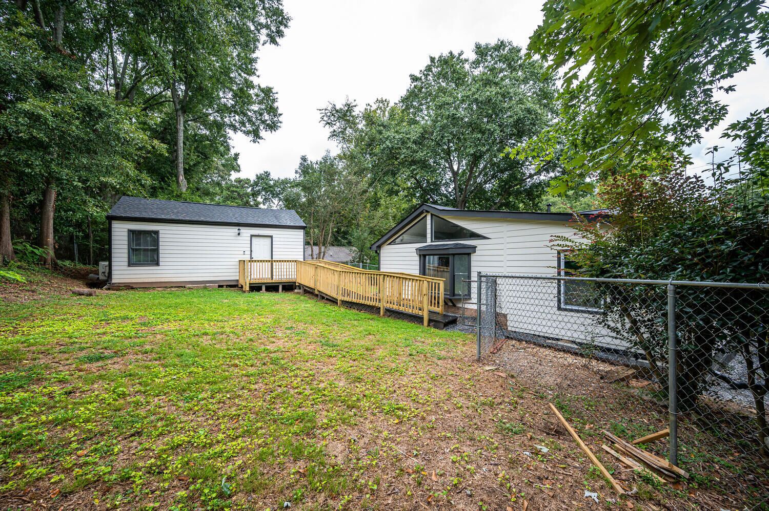 A small, single-story cabin with a fenced yard, a wooden deck, and a small shed.