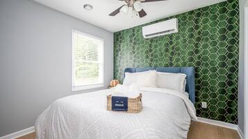 A bedroom with a bed, a ceiling fan, a window, and a wall-mounted air conditioner.