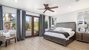 A modern bedroom with a large bed, a ceiling fan, and a view of a landscaped area. - Serene in Scottsdale-5BR w/Pool, Hot Tub + Gym (Scottsdale)