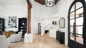 A spacious living area with a high ceiling, a staircase, and a large arched window. - Serene in Scottsdale-5BR w/Pool, Hot Tub + Gym (Scottsdale)