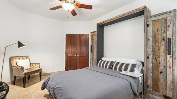 A bedroom with a bed, a chair, a wardrobe, a ceiling fan, and a floor lamp. - Serene in Scottsdale-5BR w/Pool, Hot Tub + Gym (Scottsdale)