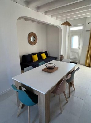 Un coin repas avec une table blanche, des chaises en bois et un canapé noir et jaune en arrière-plan.
