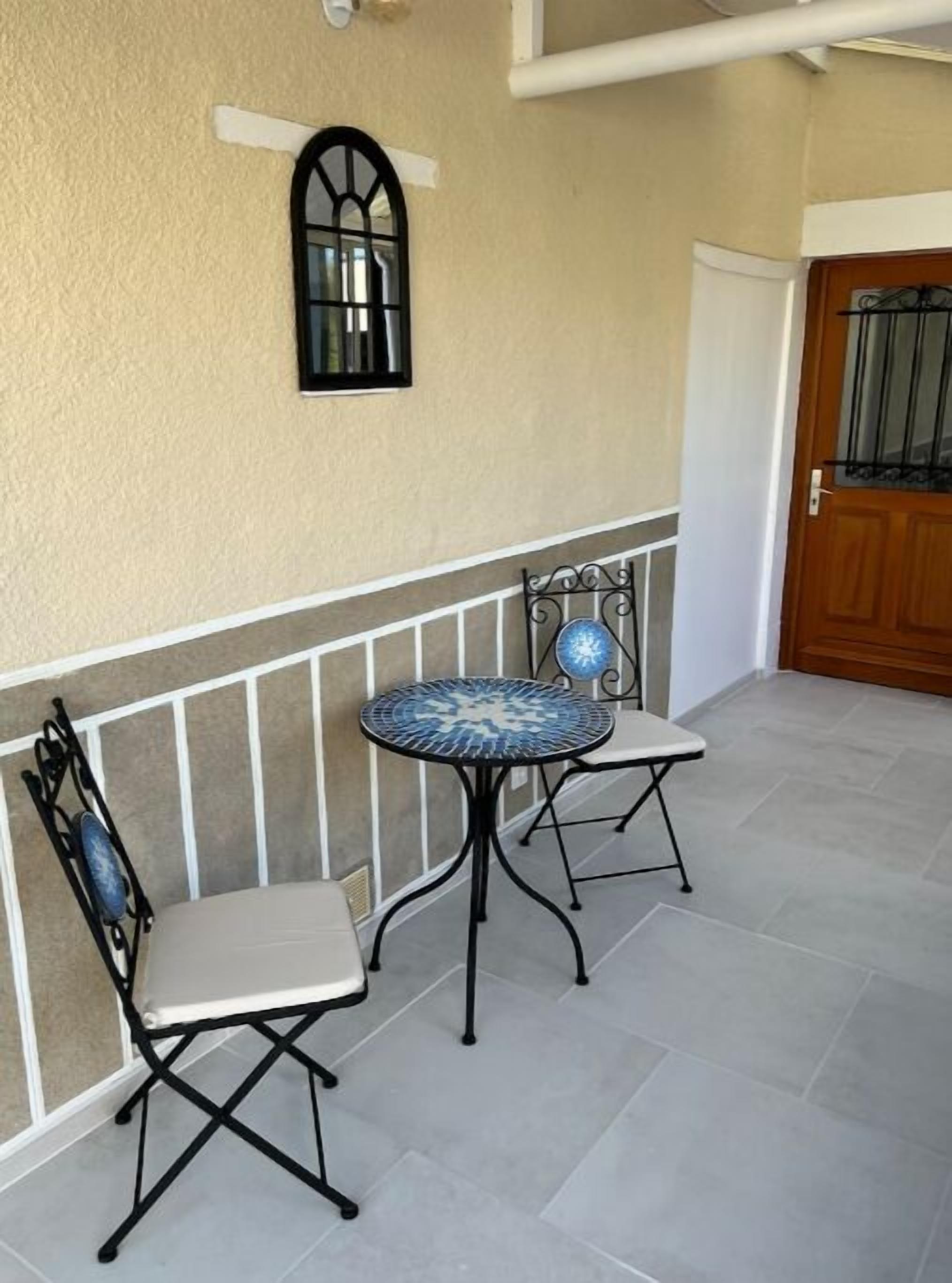 Un pequeño patio con dos sillas y una mesa, un adorno fijado a la pared y una puerta con ventana.
