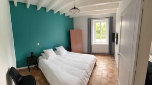 A bedroom with a teal wall, a large bed, a wooden chair, a wardrobe, and a window with curtains.