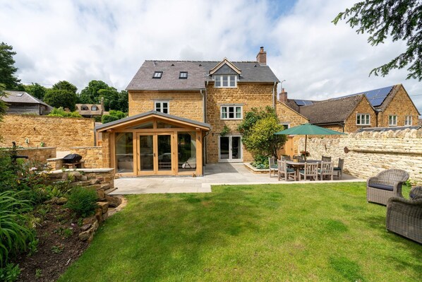 Une maison en pierre avec un grand jardin, un patio couvert et un coin repas aménagé avec du mobilier d’extérieur.