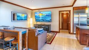 A modern living room with a large TV, a sofa, a coffee table, and a bar area.