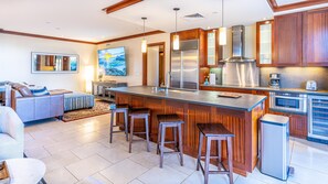 A modern kitchen with a large island, bar stools, stainless steel appliances, and wooden cabinetry.