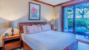 A neatly made bed with a white comforter and floral pillows, a wooden headboard, a bedside table with a lamp, and a digital clock.