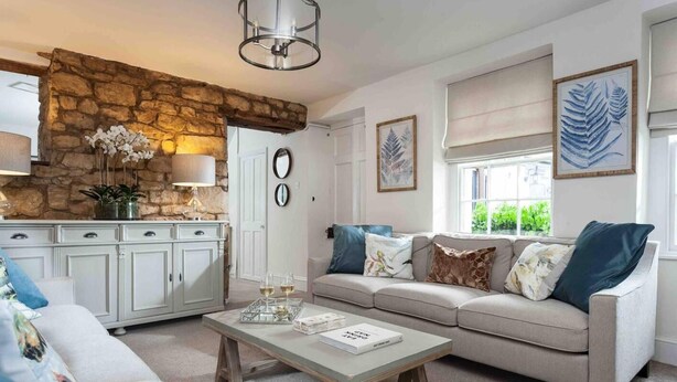 A living room with a stone wall, a sofa, a coffee table, and a dining area with cabinets. - Beautiful Cotswold Cottage in Rodborough, Stroud (Stroud)