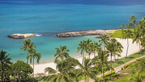 Una playa tropical con aguas turquesas cristalinas, palmeras y un rompeolas rocoso.