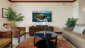 Una sala de estar con una mesa de centro redonda negra, un sofá, dos sillones, un mueble de madera y un cuadro grande con un paisaje costero.