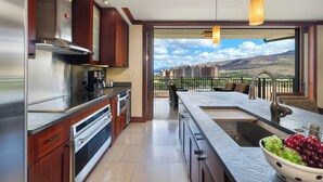 Una cocina moderna con una isla grande, electrodomésticos de acero inoxidable y vistas a un paisaje montañoso desde un balcón.