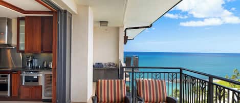 A balcony with wicker furniture, a glass table, and a view of the ocean.