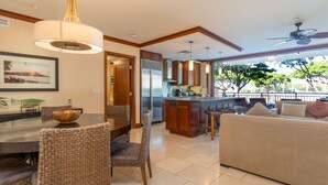 Una cocina moderna con una isla central, armarios de madera y un comedor con sillas de mimbre.